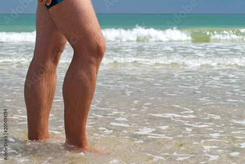 young man feet close-up swimming trunks walking sea shore, wave horizon water, summer rest beach weekend vacation