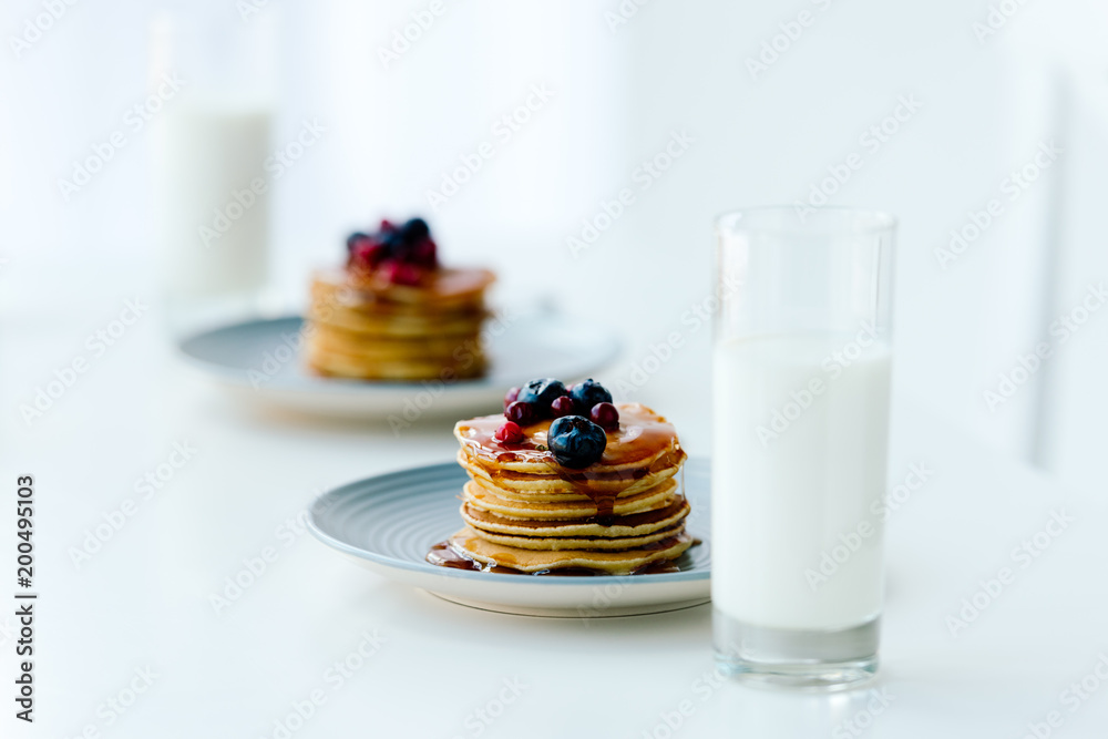 selective focus of homemade pancakes with berries and honey and glasses of milk on tabletop selective focus of homemade pancakes with berries and honey and glasses of milk on tabletop