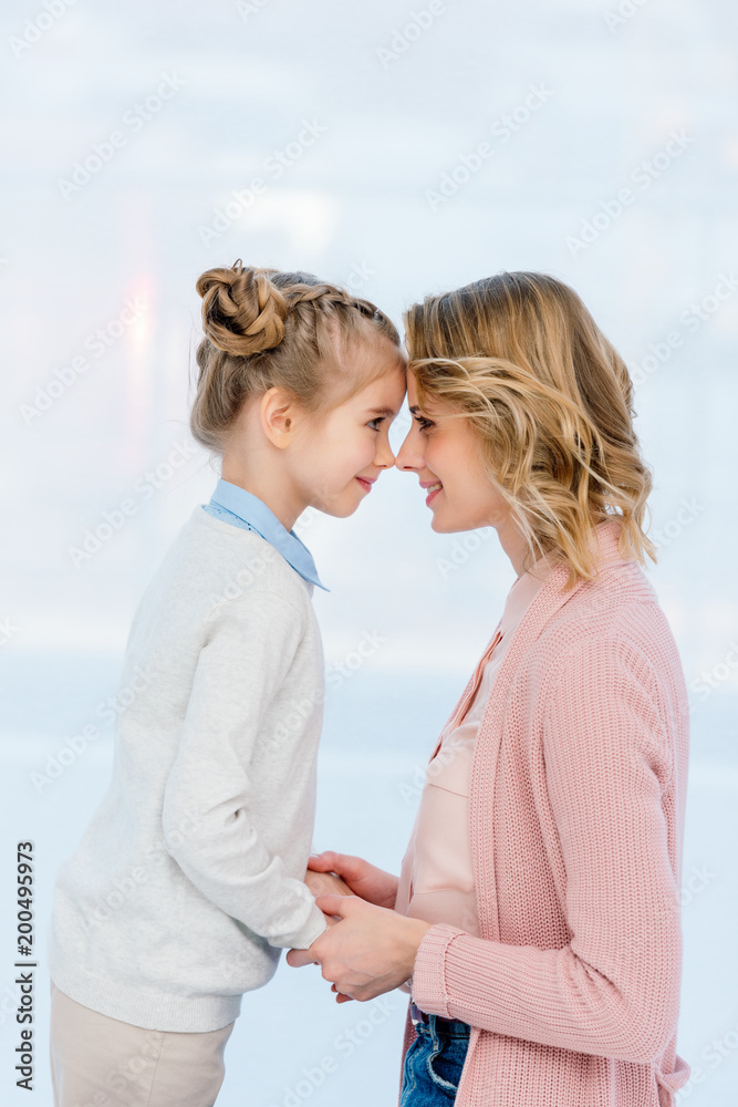 side view of mother and daughter touching with foreheads at home side view of mother and daughter touching with foreheads at home