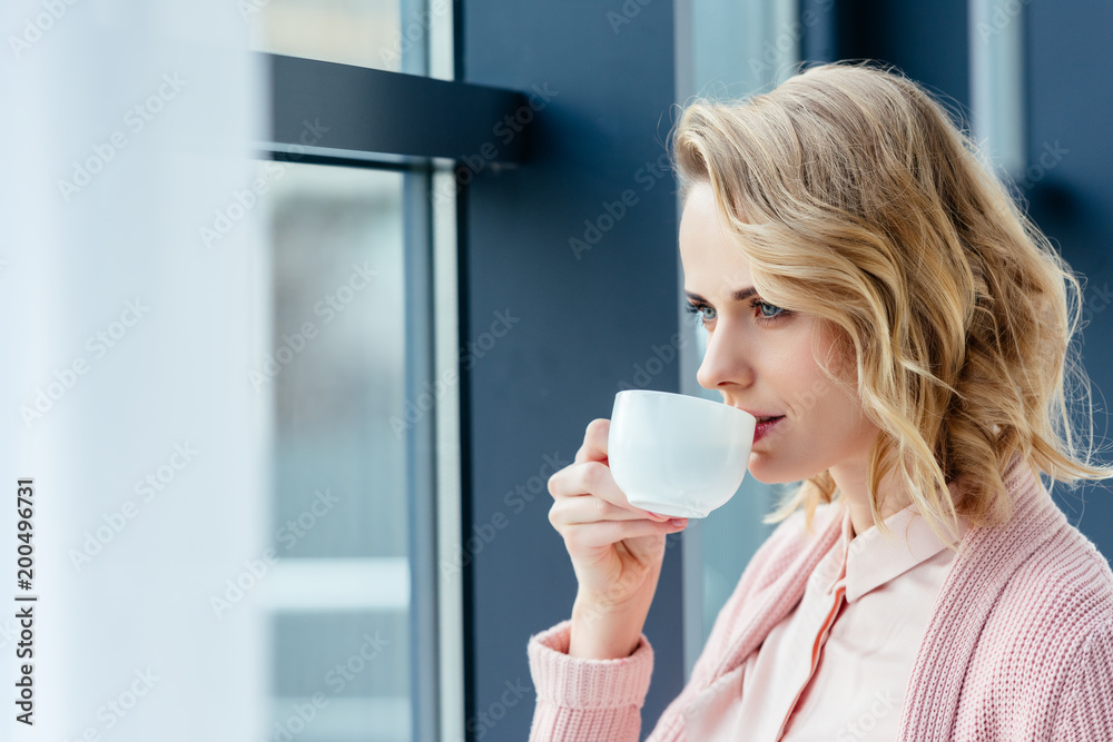 side view of thoughtful woman drinking coffee and looking out window side view of thoughtful woman drinking coffee and looking out window