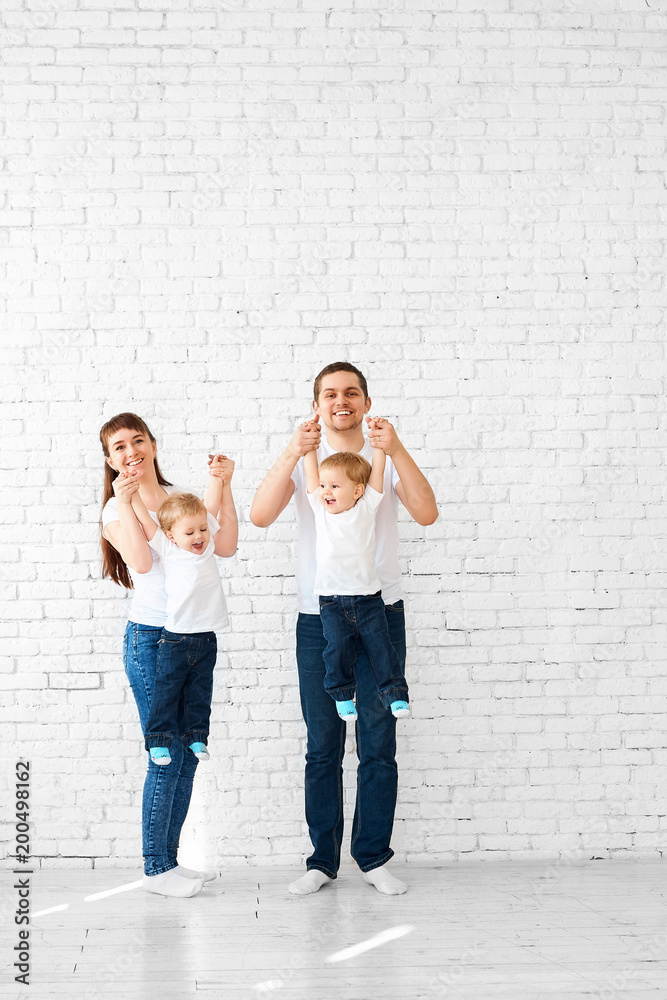 Happy young family with twins having fun playing on a white brick wall background, hugging each other and smiling Happy young family with twins having fun playing on a white brick wall background, hugging each other and smiling