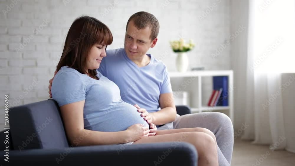 pregnant woman and her husband sitting on a sofa and touching pregnant tummy pregnant woman and her husband sitting on a sofa and touching pregnant tummy