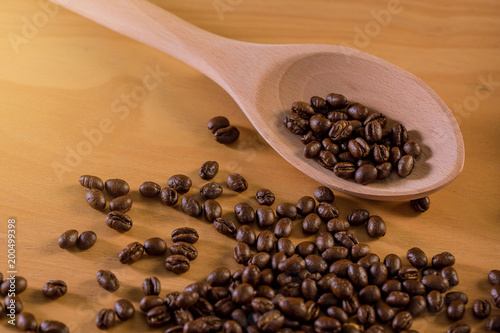 The roasted coffee beans are placed on a wooden ladle on a patterned wooden floor.