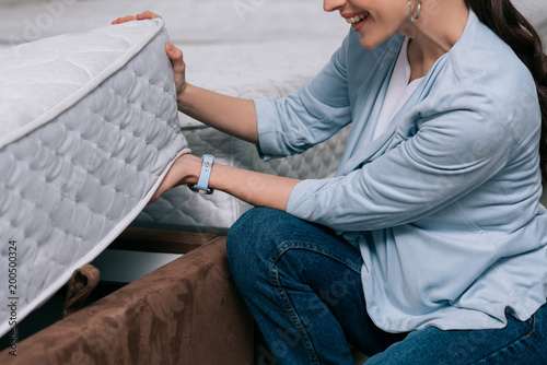cropped shot of smiling woman choosing orthopedic mattress in furniture store