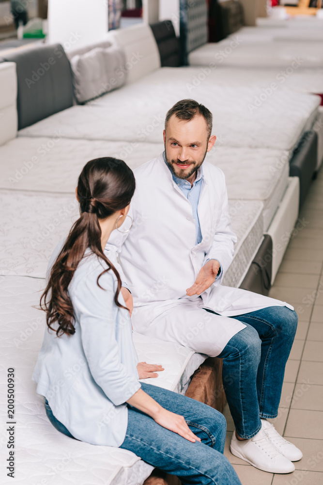 shop assistant in white coat and female customer in furniture store with arranged mattresses shop assistant in white coat and female customer in furniture store with arranged mattresses