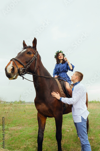 happy girl is sitting on a horse and her boyfriend stands next to her looking at her © Ivan