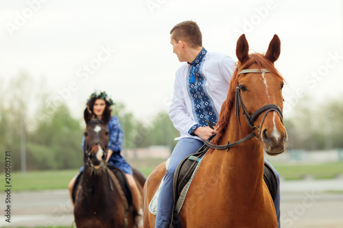 The guy rides on a horse and looks at his girlfriend who rides a horse behind him