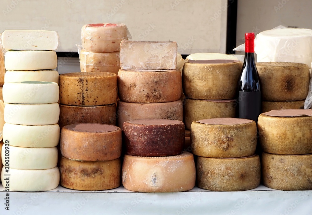Cheese wheels of Pecorino and Sardinian ricotta in different stacks on a shelf of an outdoor market. A bottle of red wine Cannonau in the middle Cheese wheels of Pecorino and Sardinian ricotta in different stacks on a shelf of an outdoor market. A bottle of red wine Cannonau in the middle