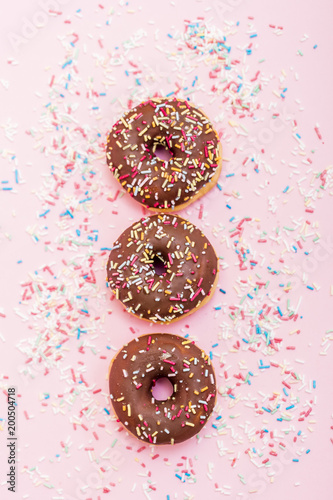 chocolate donuts with colorful sprinkles on pink background