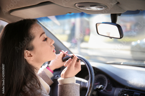 Young woman applying makeup in car during traffic jam