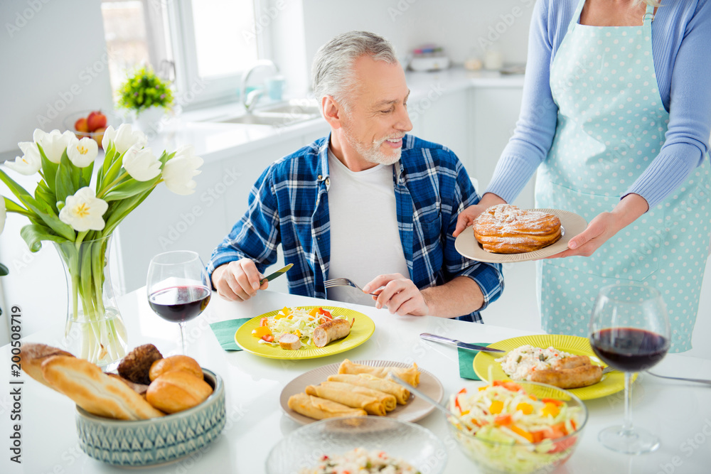 Handsome man with bristle sitting at the table eating food having glass of red wine, woman holding in hands plate demonstrate tasty sweet baked bun to her lover, lovely couple enjoying dinner indoor