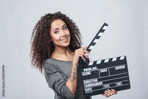 Smiling curly female holding movie clapper board, slate film.