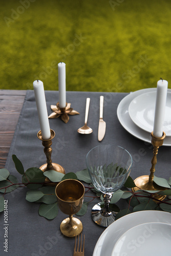 close up view of rustic table arrangement with winecups, eucalyptus, vintage cutlery, candles in candle holders and empty plates photo