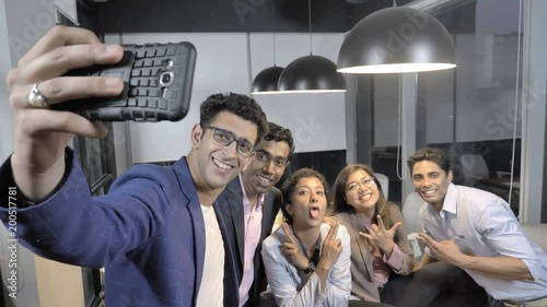 A young businessman taking a selfie photo on smartphone with a his positive and energetic team members. A startup business team members taking a selfie picture after achieving their target of goal photo