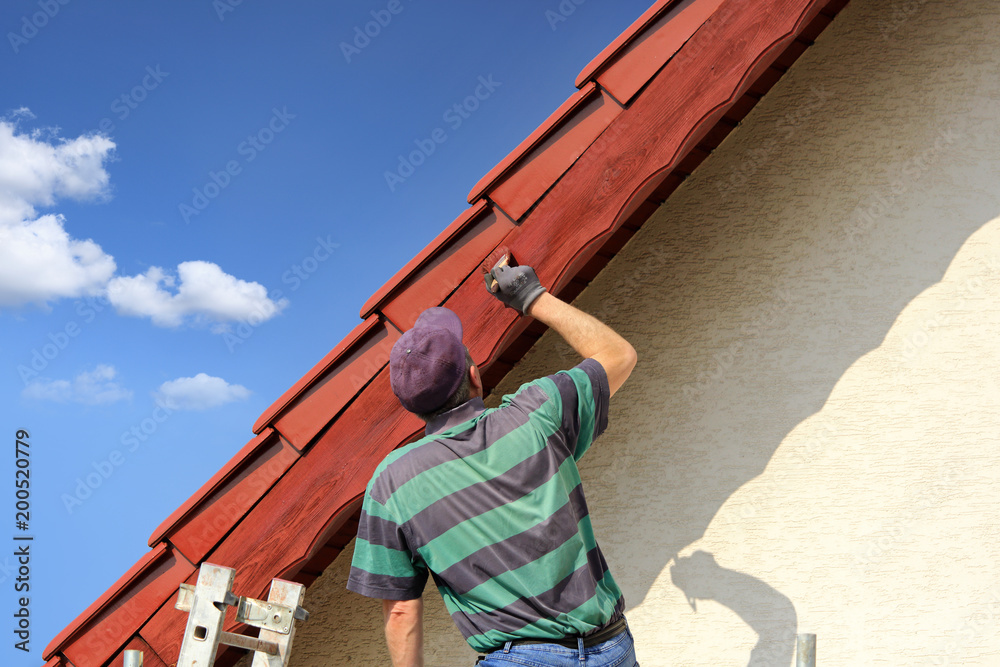 Mężczyzna, malarz maluje farbą okap czerwoego dachu. - obrazy, fototapety, plakaty 