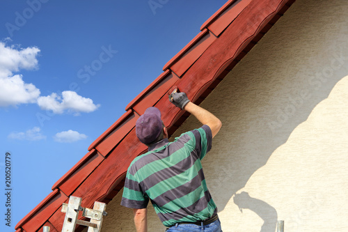 Mężczyzna, malarz maluje farbą okap czerwoego dachu.