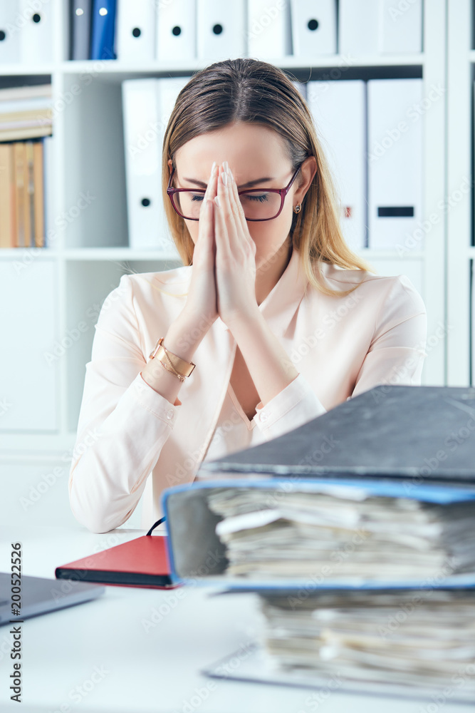 Close up stressed office woman doing praying hand gesture while looking at the pile of documents at her workplace. Close up stressed office woman doing praying hand gesture while looking at the pile of documents at her workplace.
