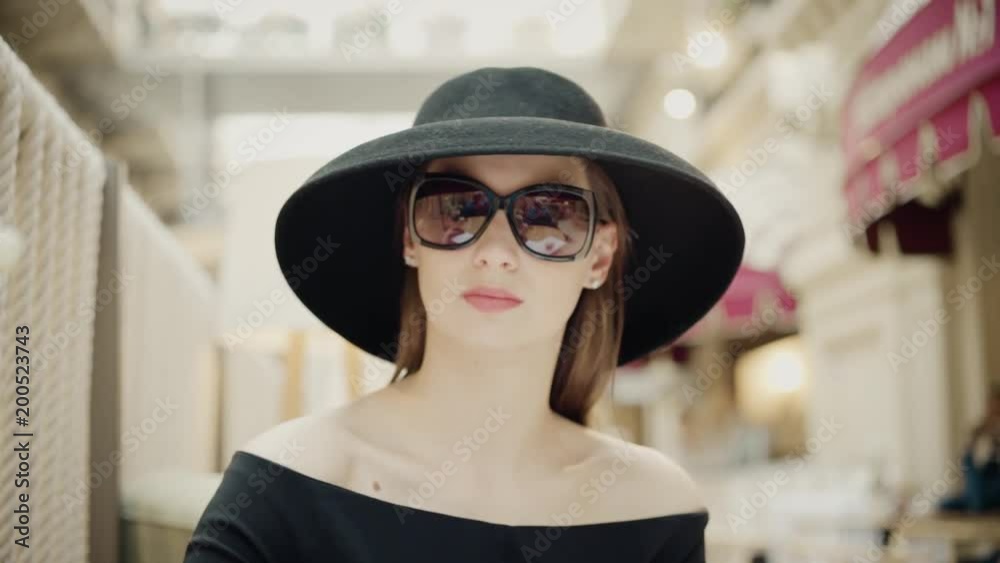 Portrait of fashionable woman in a black hat sits in a summer cafe and wears sunglasses. Slow motion Portrait of fashionable woman in a black hat sits in a summer cafe and wears sunglasses. Slow motion