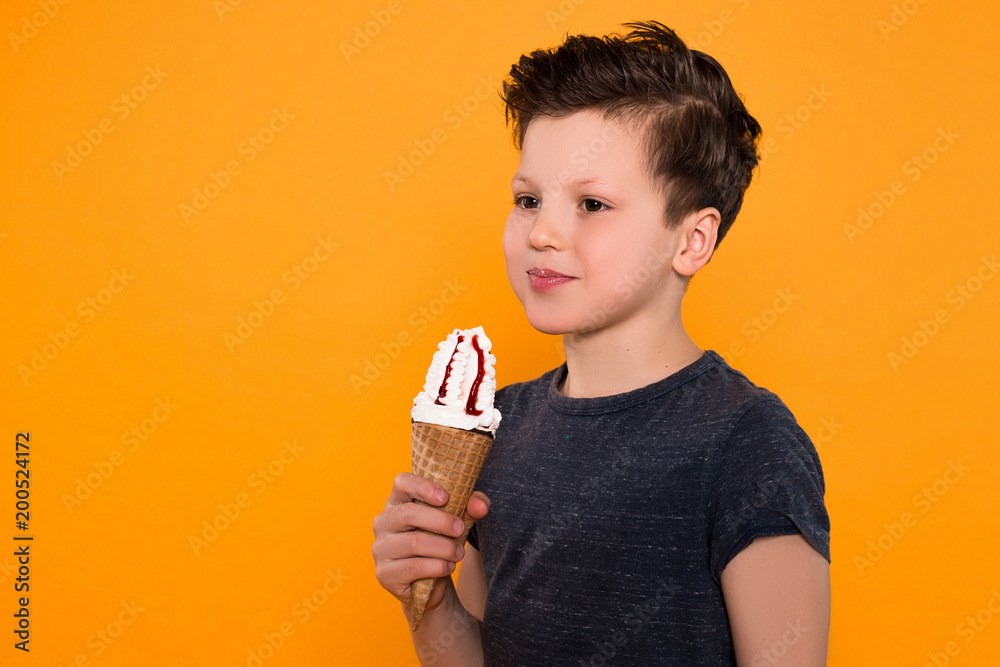 Spend time with pleasure! Close up portrait of the delighted little child with ice-cream cone posing at the camera over orange background. Spend time with pleasure! Close up portrait of the delighted little child with ice-cream cone posing at the camera over orange background.