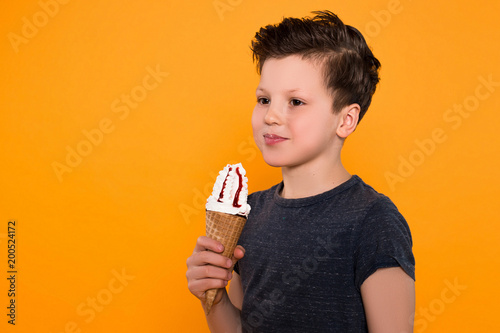 Spend time with pleasure! Close up portrait of the delighted little child with ice-cream cone posing at the camera over orange background.