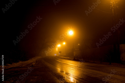 The road at night illuminated by dim lanterns during a thick fog  