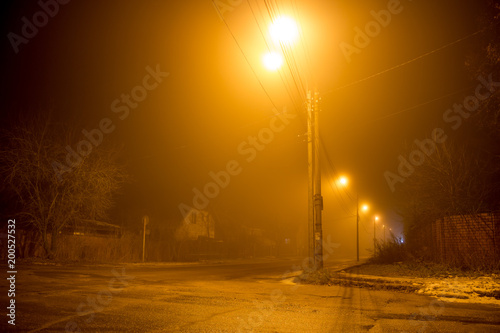 The road at night illuminated by dim lanterns during a thick fog 