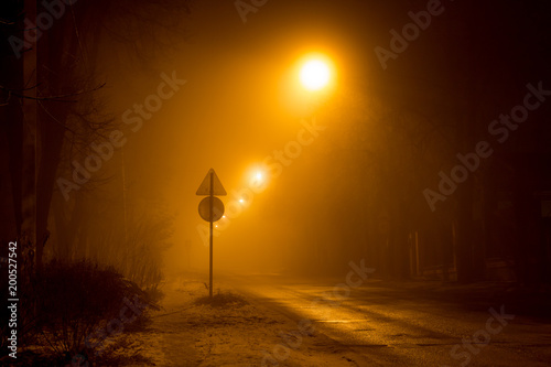 The road at night illuminated by dim lanterns during a thick fog 