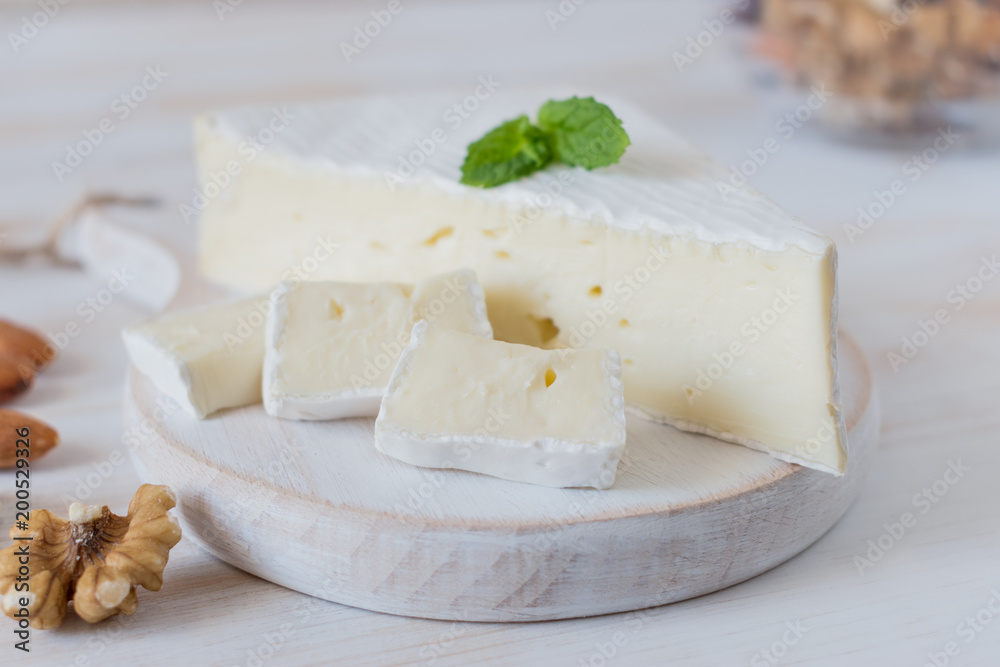 Fresh Brie cheese and a slice on a wooden board with nuts