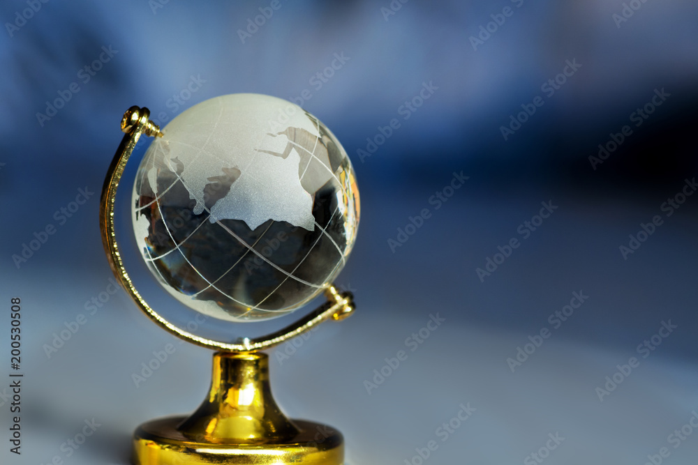 Glass globe on a stand on a blue background with rays. Planet earth globe with continents figurine on table Glass globe on a stand on a blue background with rays. Planet earth globe with continents figurine on table