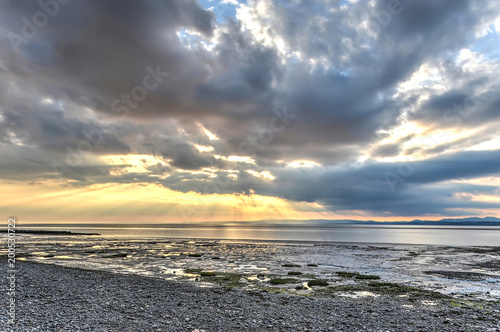 The rays of the late afternoon sun break through the clouds over the waters and adjacent mudflats of the bay of Morecambe  Lancashire  England