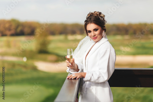 The bride is holding a glass of champagne. wedding morning. Happy and smiling girl. Outdoors photo