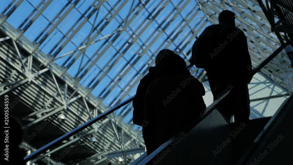 Commerce concept: customers figure elevated on the luxury department market centre. Male and female persons on the moving steps in modern hallway with beautiful view with blue sky from the ceiling Commerce concept: customers figure elevated on the luxury department market centre. Male and female persons on the moving steps in modern hallway with beautiful view with blue sky from the ceiling