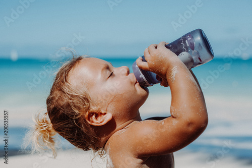 Kind trickt genüsslich aus einer Flasche am Strand photo