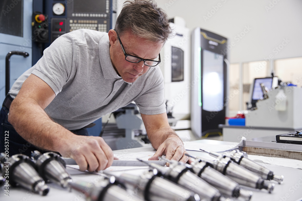 Male Engineer Measuring CAD Drawings In Factory Male Engineer Measuring CAD Drawings In Factory