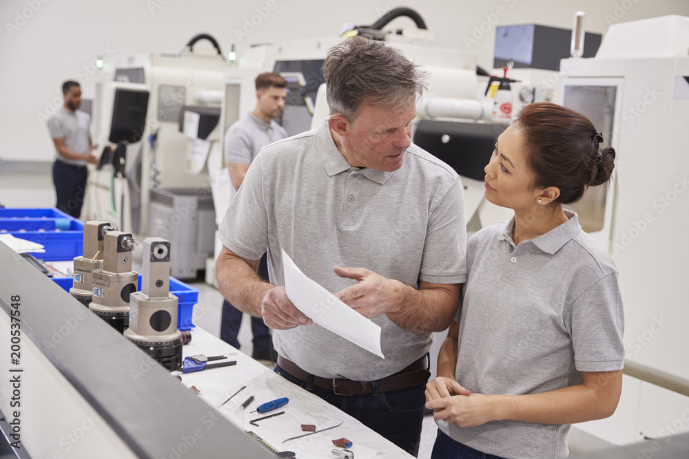Obraz premium Engineer And Female Apprentice Discussing Job Sheet In Factory
