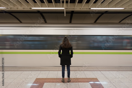 Young woman in black coat at the underground platform, waiting for a train.