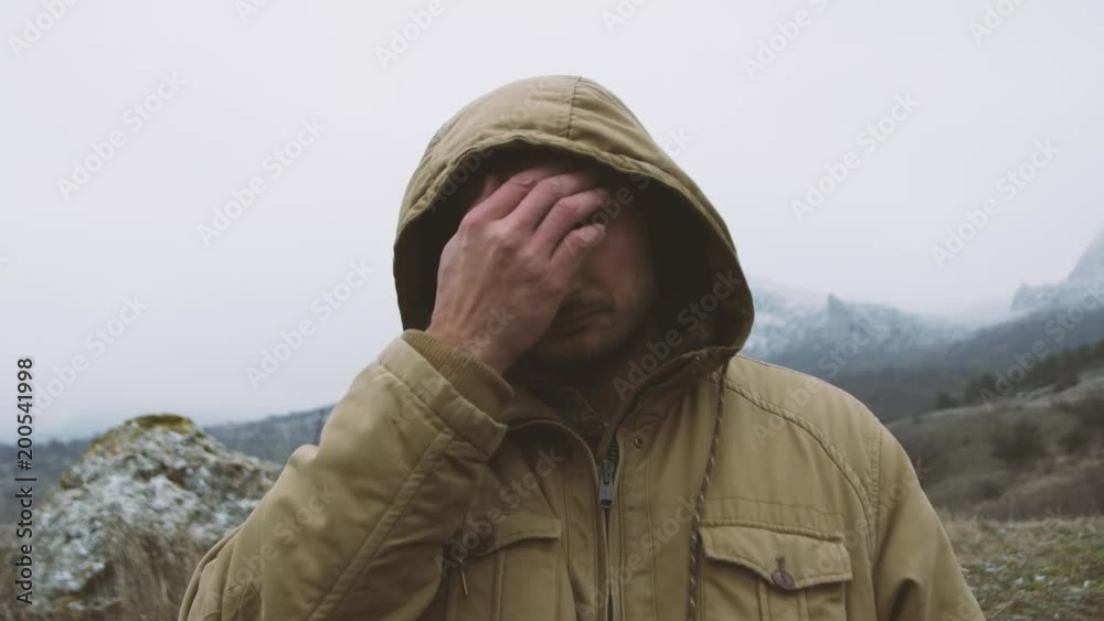 the man in the hood wipes his eyes against the background of the mountains the man in the hood wipes his eyes against the background of the mountains