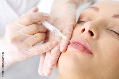 Powiększanie ust. Kosmetyczka ostrzykuje twarz kobiety podczas zabiegu odmładzającego w klinice piękności.