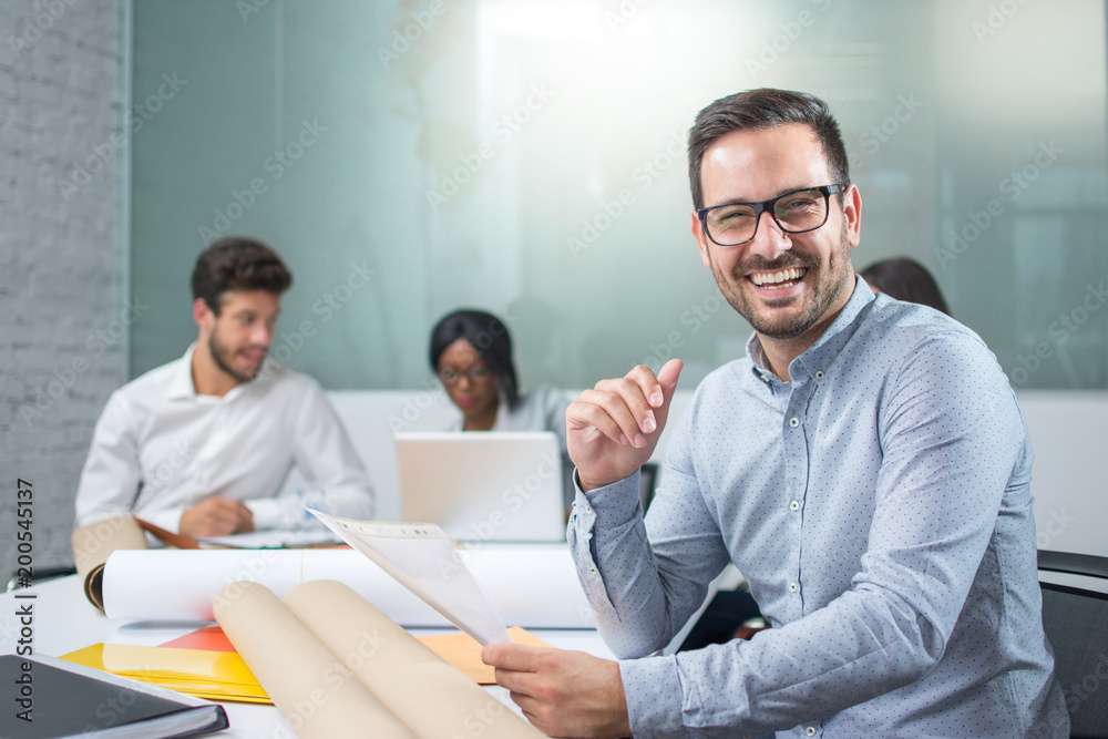 Portrait of smiling young businessman holding paper document and looking at camera in office Portrait of smiling young businessman holding paper document and looking at camera in office