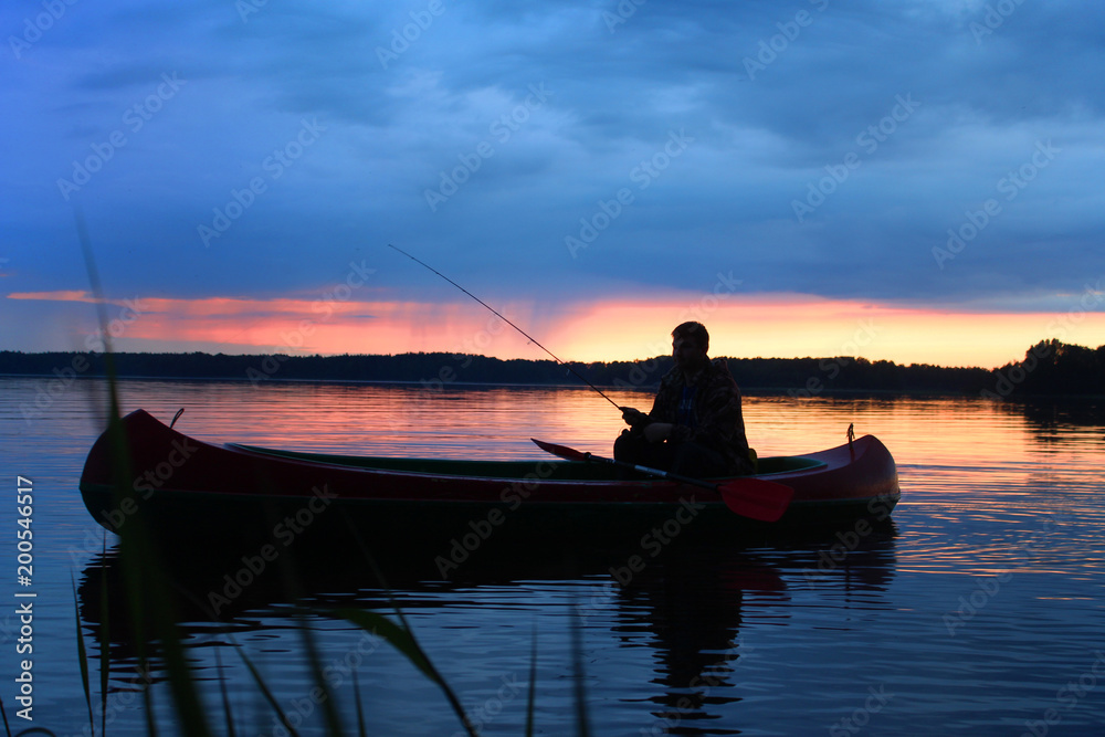 Sunset on the Vuoksa lake and silhouette of a fisherman in a boat.
