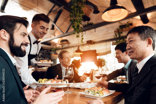 Meeting with chinese businessmen in restaurant. Waiter is bringing sushi.
