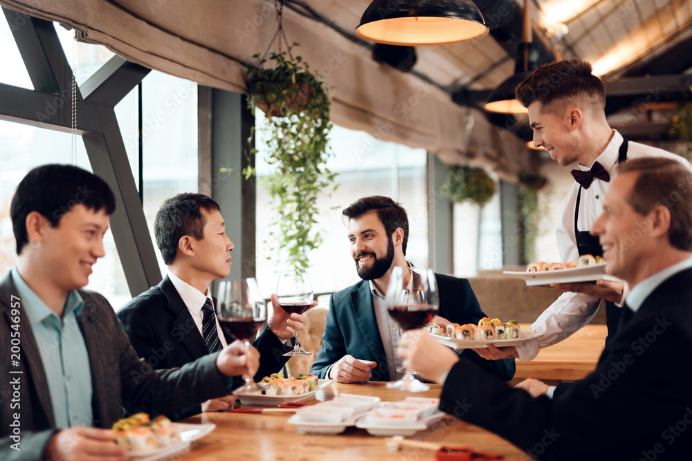 Meeting with chinese businessmen in restaurant. Waiter brings sushi. Meeting with chinese businessmen in restaurant. Waiter brings sushi.