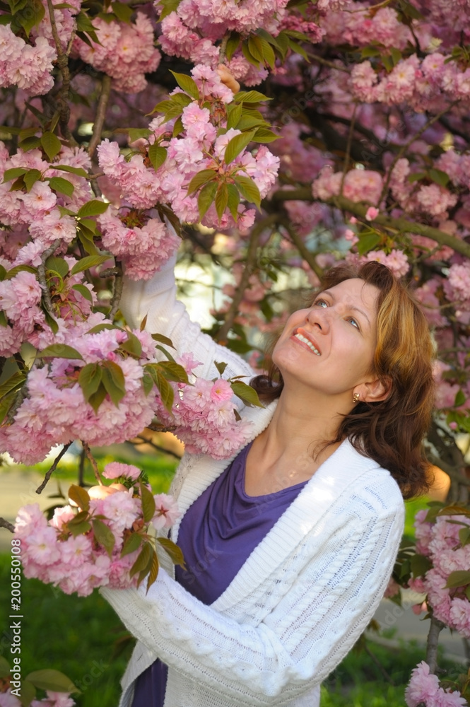 Fototapeta premium A woman with a beautiful smile is happy in the spring. She enjoys the flowering of sakura