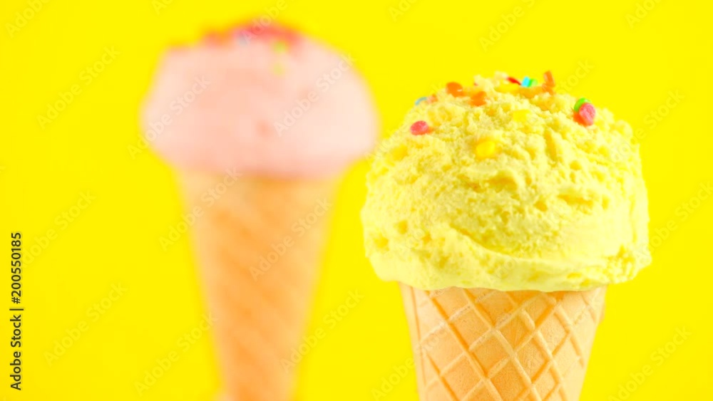 Ice cream. Vanilla, banana or lemon flavor icecream in waffle cone rotated over yellow background. Sweet dessert decorated with colorful sprinkles closeup. 4K UHD video footage. 3840X2160 Ice cream. Vanilla, banana or lemon flavor icecream in waffle cone rotated over yellow background. Sweet dessert decorated with colorful sprinkles closeup. 4K UHD video footage. 3840X2160