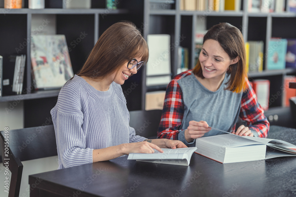 Fototapeta premium Smiling girls with laptop in a bookstore