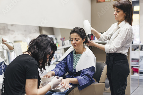 Young beautiful woman in a beauty salon while the hairdresser arranges her hair and gets her a manicure