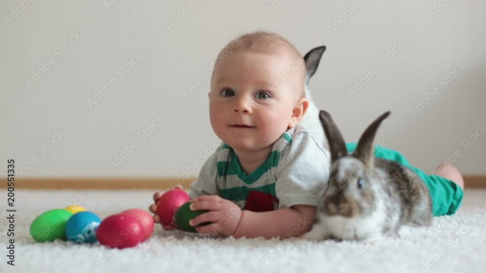 Little toddler child, baby boy, playing with bunnies and easter eggs at home, colorful hand drawings on the eggs Little toddler child, baby boy, playing with bunnies and easter eggs at home, colorful hand drawings on the eggs