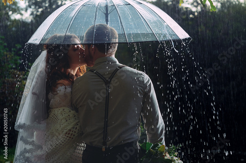 Wedding couple waking by the rain under umbrella
