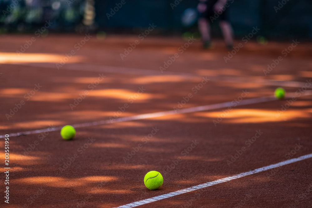 Tennis balls on a clay court in the foreground. Blurred player in the background