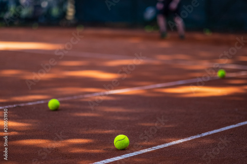 Tennis balls on a clay court in the foreground. Blurred player in the background